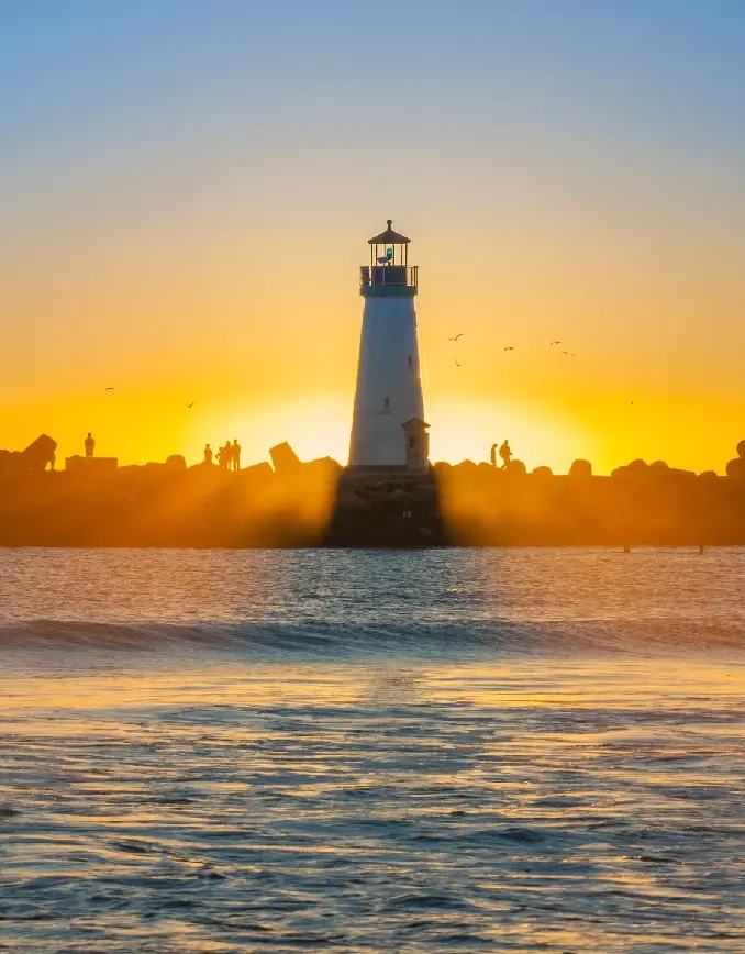 A lighthouse is shown in the distance as the sun sets.