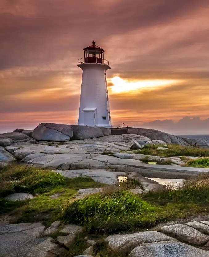 A lighthouse on the rocks at sunset.